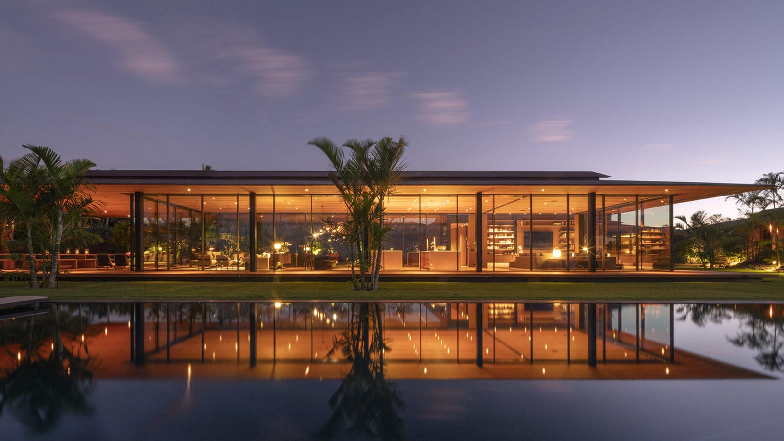 Glass-walled pavilion beside a reflecting pool at dusk